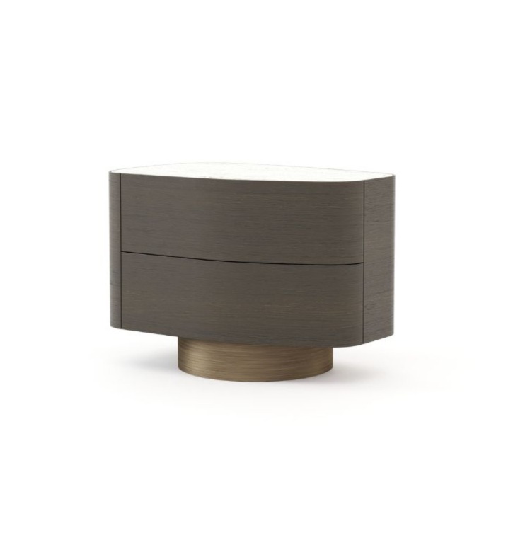 The Stone Night Table, crafted from dark wood with two rounded drawers and a smooth white stone top, rests on a circular base in brushed bronze and is displayed in a minimalist setting that highlights its oval silhouette.