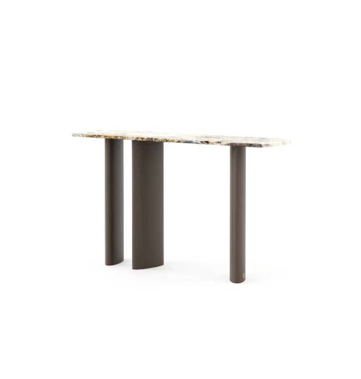 The Dolomites Console is shown as a modern console table with a stone‑like top featuring natural veining, supported by three dark cylindrical legs arranged asymmetrically, placed in a minimalist interior with warm tones and decorative objects on the surface.