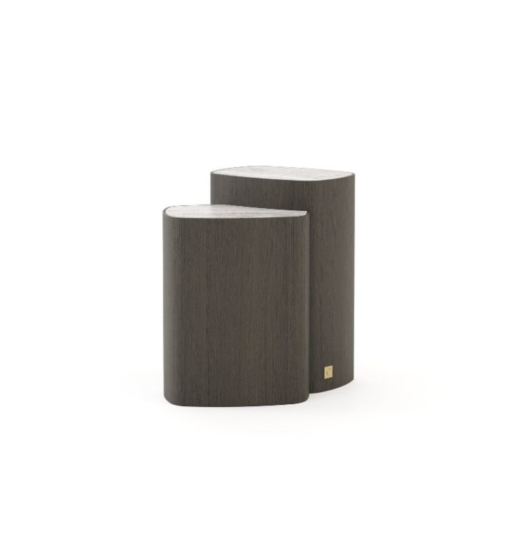 The Dolomites Side Table is shown as a pair of sculptural wooden tables with an organic rounded‑triangular form in a dark finish, one slightly taller than the other, featuring a small brass detail near the base and placed together in a minimalist interior.