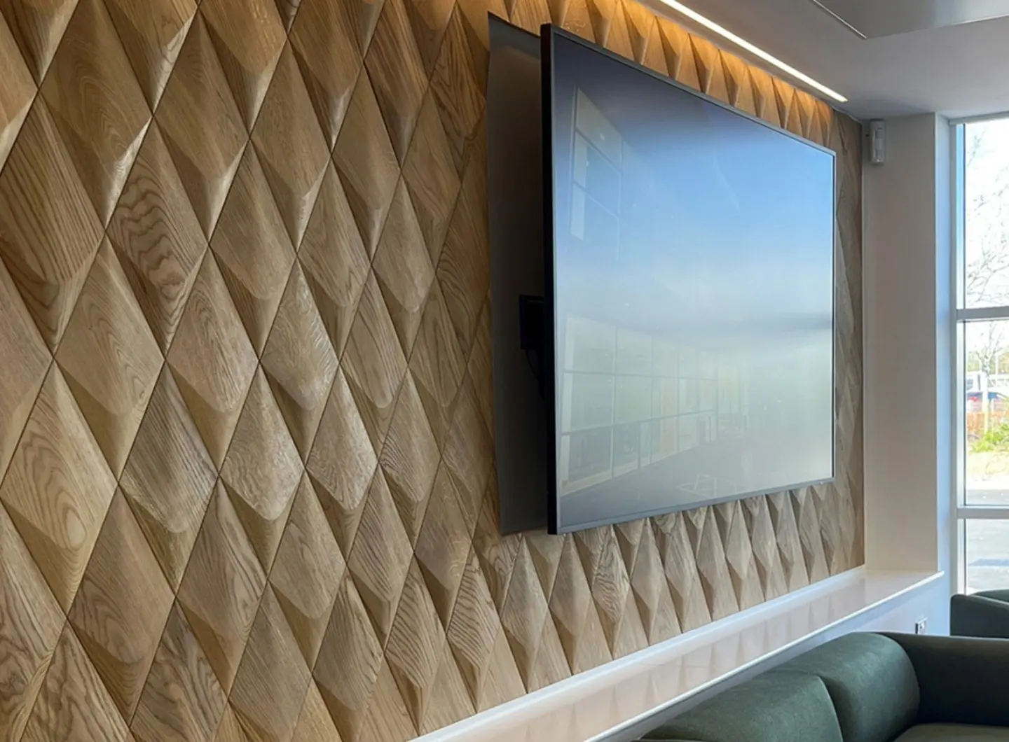 Modern office media wall featuring 3D oak wood panels in a diamond pattern with a large TV screen and accent LED lighting.
