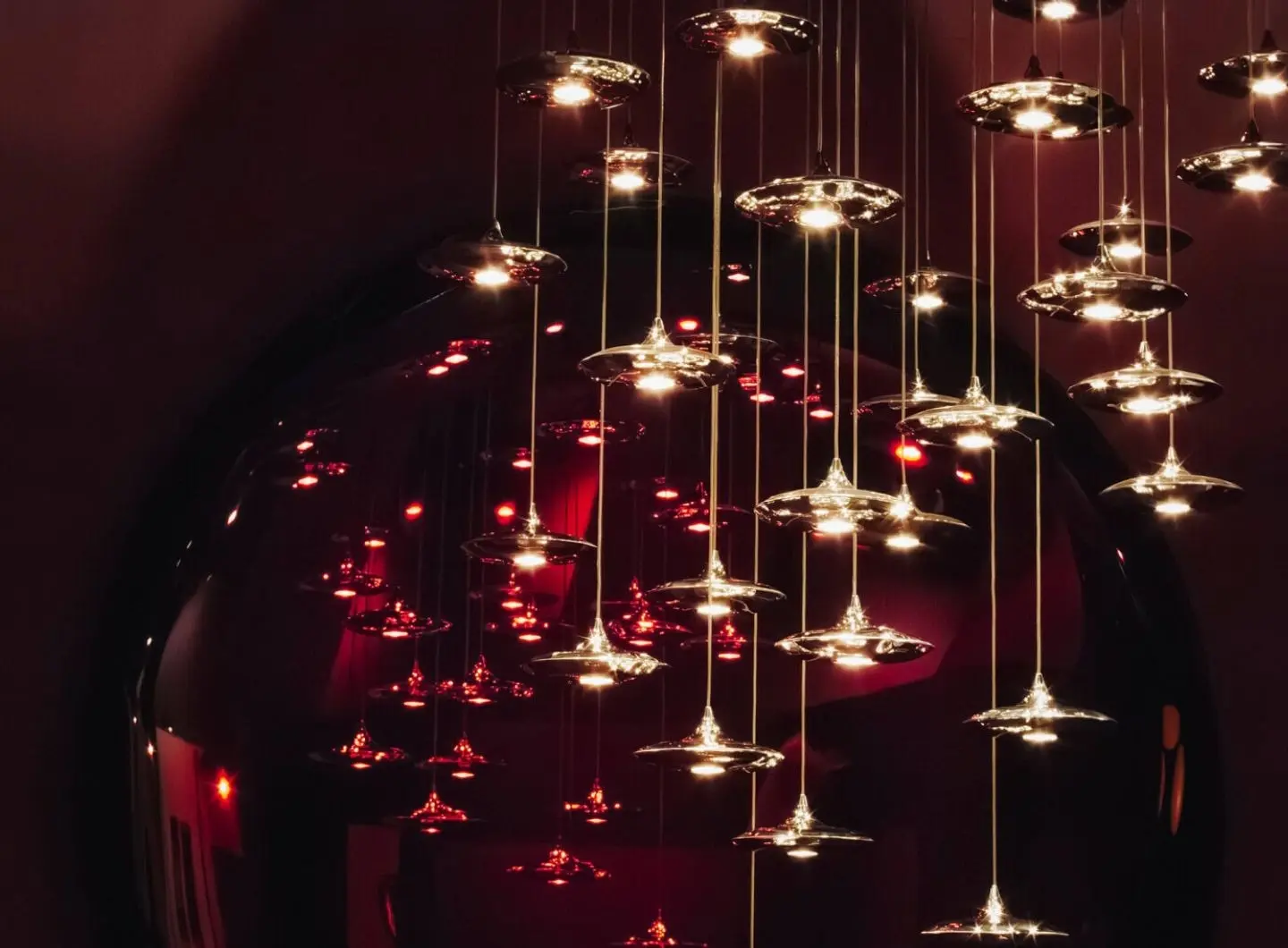 Contemporary lighting installation by Zieta Studio with suspended metal LAMPIN lamps in a deep red interior