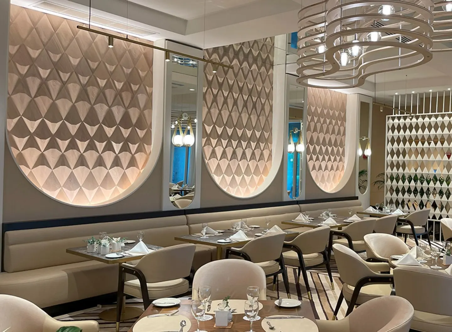 Luxury restaurant interior featuring illuminated arched niches with 3D oak wood panels in a triangle pattern, beige furniture, and mirrors.