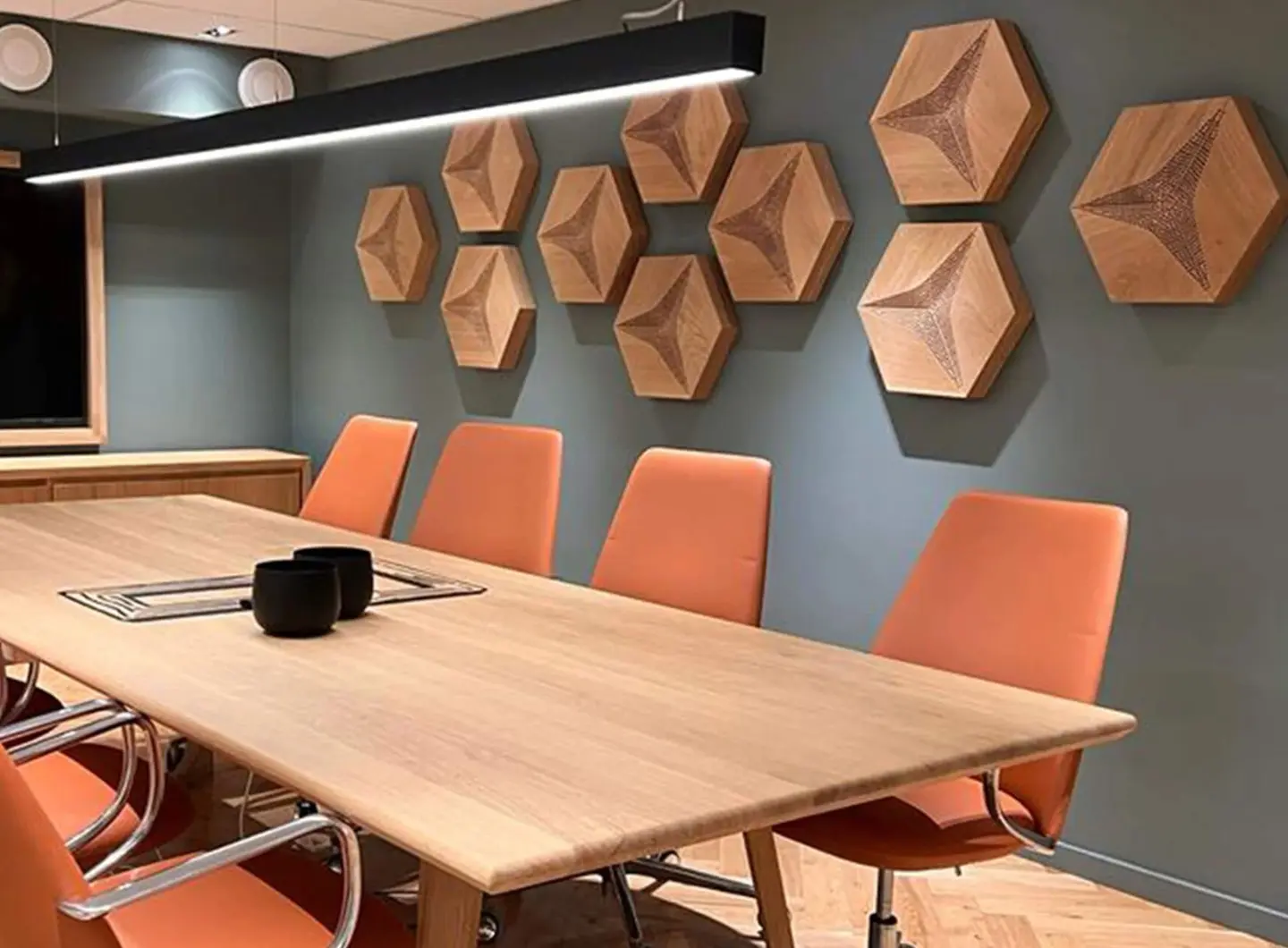 Modern meeting room featuring 3D oak acoustic panels in Hexagon pattern for soundproofing, with a wooden table and orange office chairs.