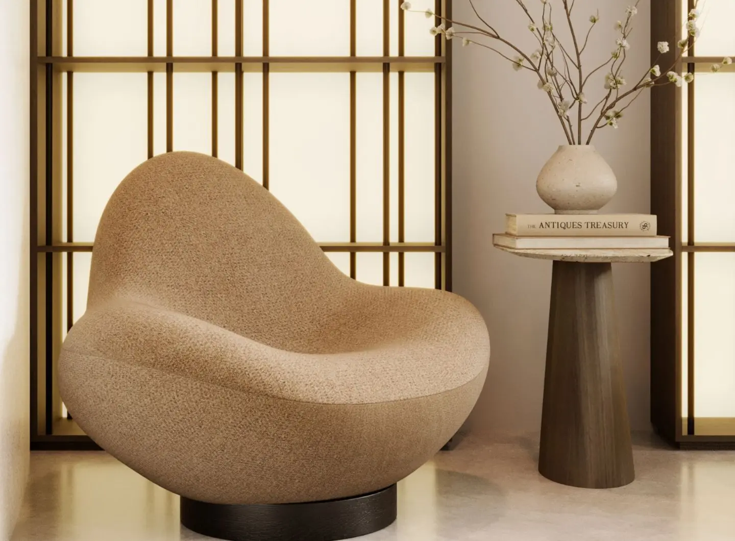 The Stone armchair, upholstered in textured beige fabric and featuring soft, rounded lines, stands next to a coffee table on which are placed some books and a ceramic vase with branches, in a warm, minimalist setting.