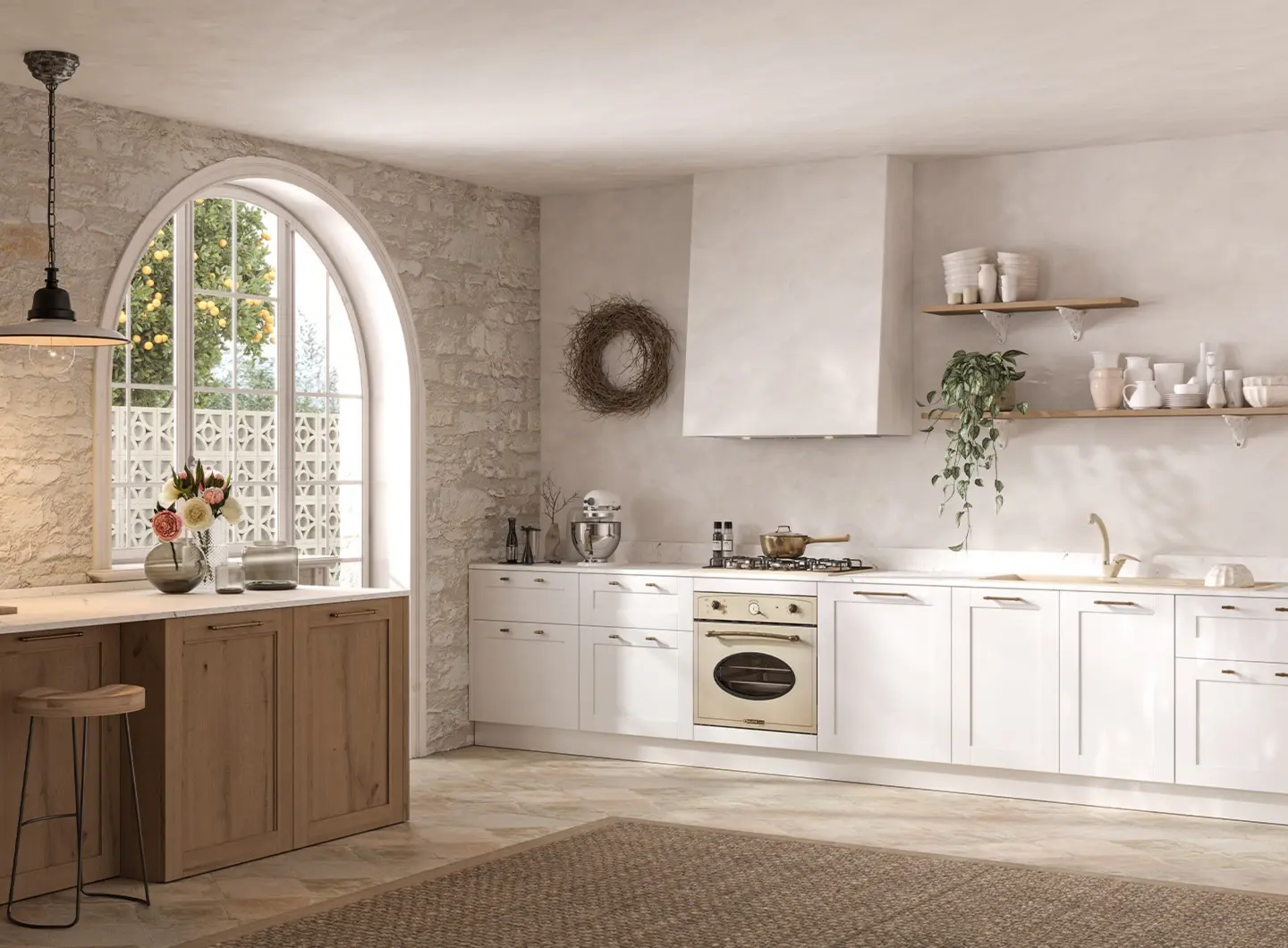 A spacious rustic-style kitchen set in a room with exposed stone walls and a large arched window. The kitchen features white cabinetry with brass shell handles, a 60 cm oven, a 70 cm traditional-style sand-colored range and an integrated extractor hood.