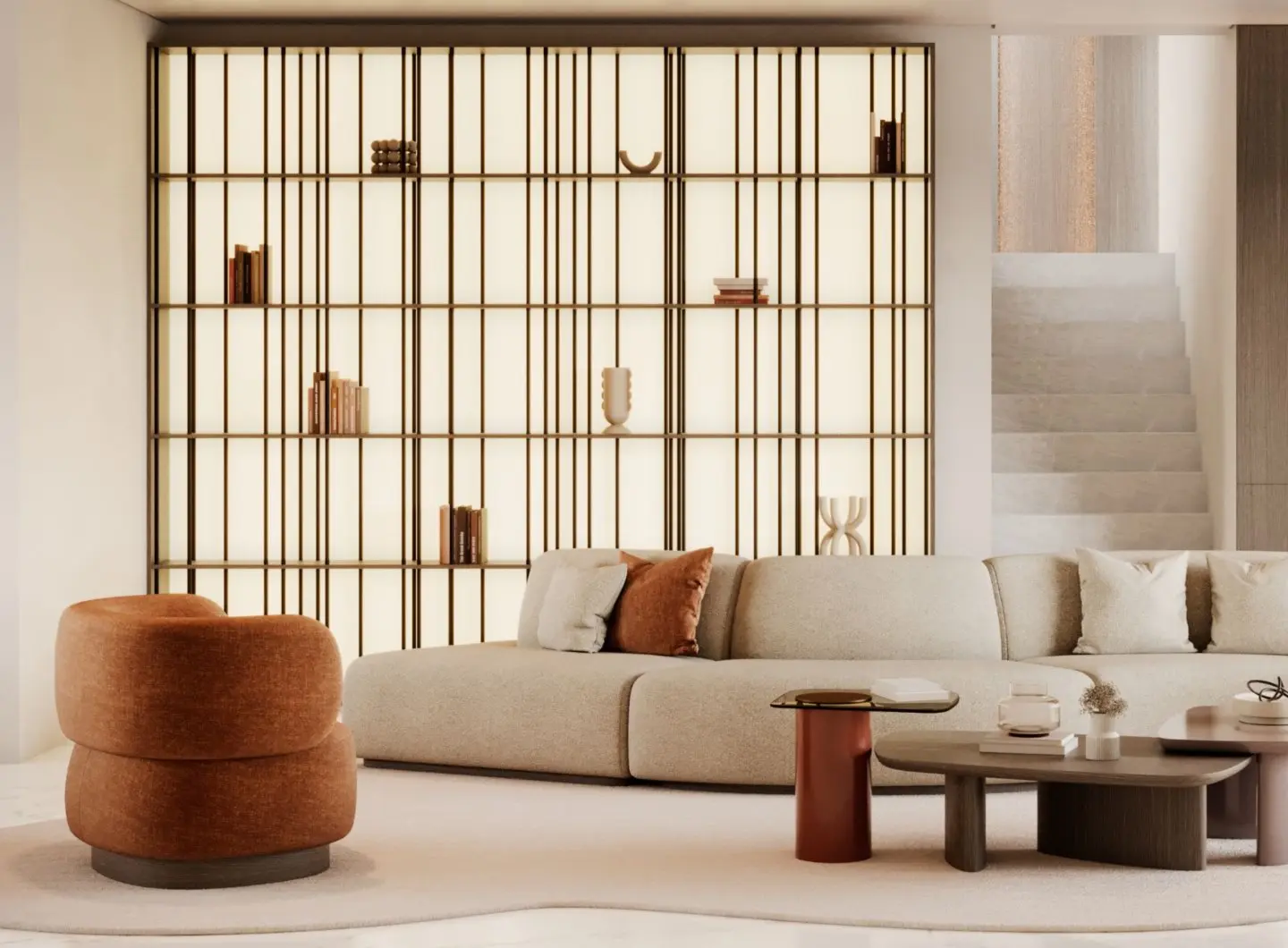 The Dolomites Armchair is placed in a warm living room, shown as a rounded upholstered chair in a light neutral tone, positioned near a sectional sofa, sculptural coffee tables, and an illuminated shelving unit within a softly lit interior.