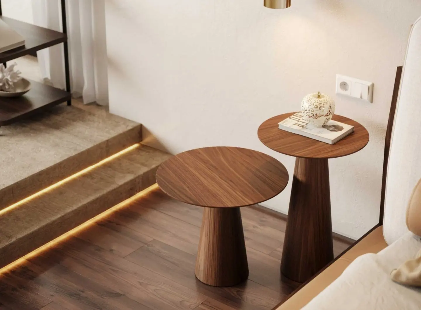 The Olivier Side Tables are displayed beside a sofa and softly lit stone steps as two round wooden tables with conical bases, one holding a decorative ceramic piece and a book, their warm tones and sculptural forms bringing understated elegance to the contemporary interior.