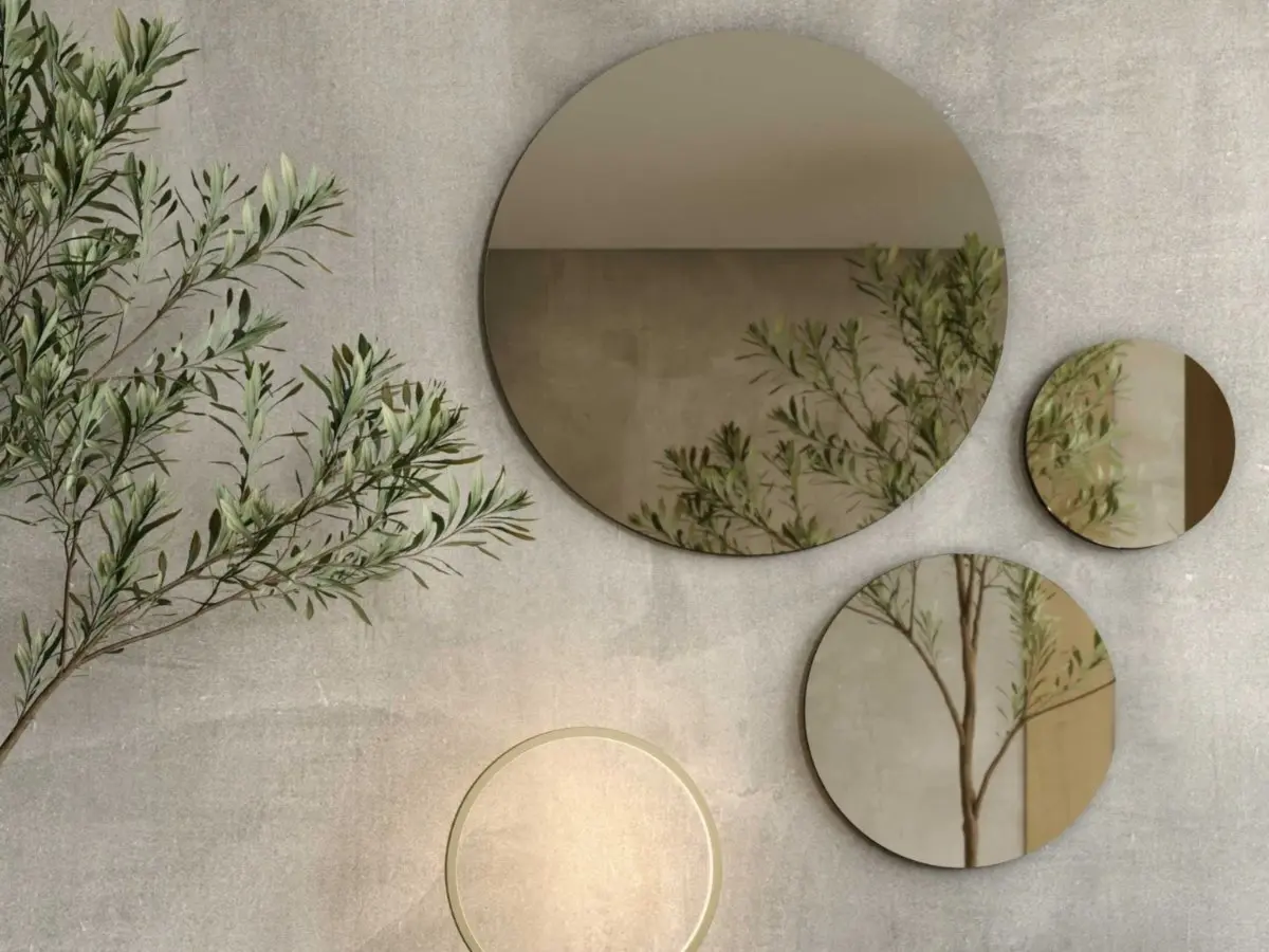 The Circle Mirror appears as part of a composition of round mirrors in varying sizes mounted on a textured grey wall, softly reflecting branches and warm light to create a serene, harmonious focal point within the space.
