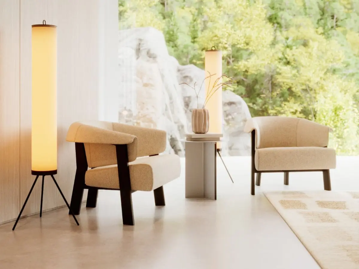 The Steel Side Table appears between two upholstered armchairs in a warm, minimalist interior, holding a decorative vase beneath soft floor‑lamp lighting, its simple round top and slender form adding a calm, understated touch to the serene seating area.