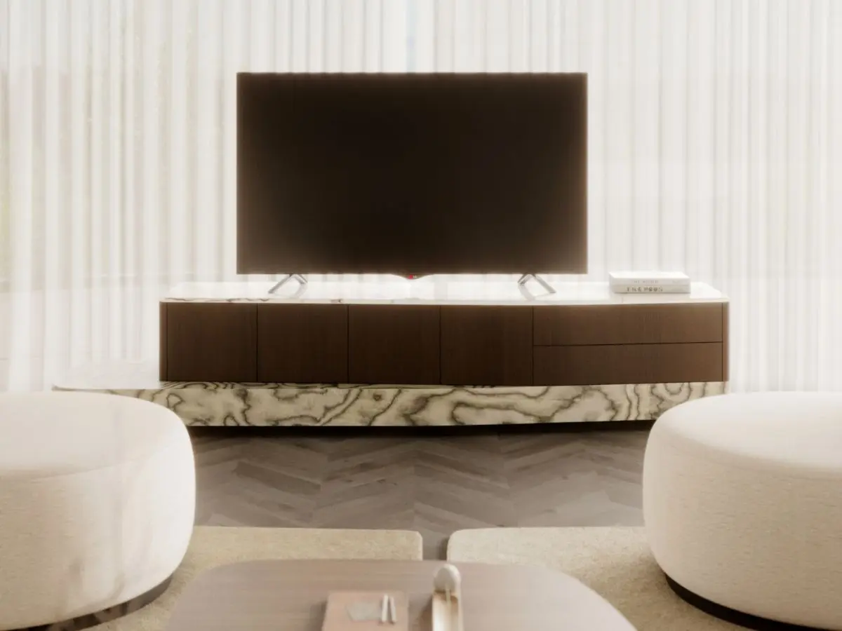 The Stone TV Cabinet appears as a long wooden media unit with a stone‑inspired base, supporting a large television, with books and decor placed on its surface, set in a bright living room with soft natural light and neutral furnishings.