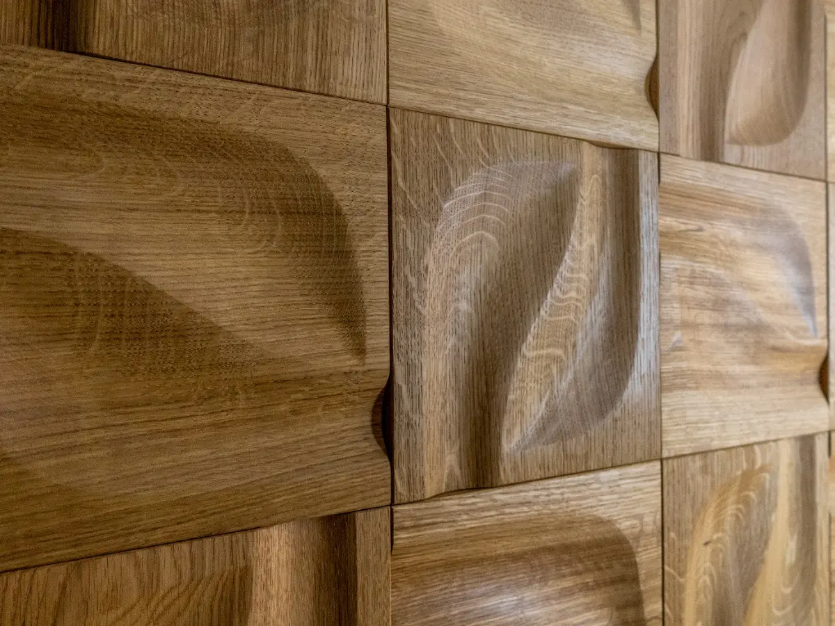 Perspective close-up of sculptural 3D oak wood wall panels with a fluid, wavy texture, showcasing natural grain and shadow play.