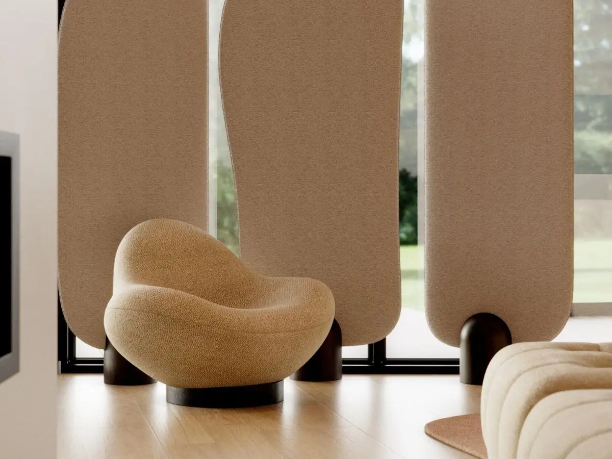 The Stone armchair, with its rounded, organic silhouette and textured beige upholstery, rests on a dark circular base in a minimalist room, where tall curved panels filter the natural light and offer a glimpse of the greenery outside.