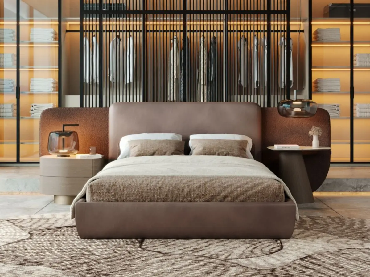 The Stone Night Table II in a large bed dressed in neutral-toned bed linen: one, in a light finish, is adorned with a glass lamp and a candle, whilst the other, in a dark finish, features a vase and a book; all set within a modern bedroom featuring an open-plan wardrobe with illuminated shelves.