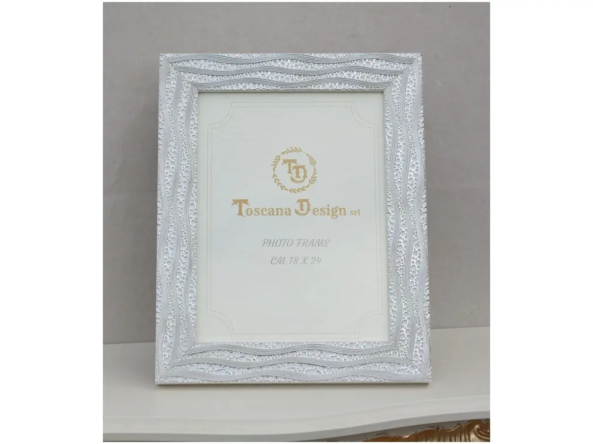 Elegant, classic-style photo frame in ivory. It features a rectangular shape with edges decorated with delicate, harmonious silver motifs. The surface has a subtle texture reminiscent of handcrafted workmanship. Suitable for 18x24 cm photographs. Ideal for refined settings, it lends a bright, sophisticated look to spaces.