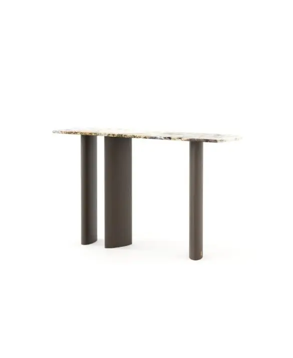 The Dolomites Console is shown as a modern console table with a stone‑like top featuring natural veining, supported by three dark cylindrical legs arranged asymmetrically, placed in a minimalist interior with warm tones and decorative objects on the surface.