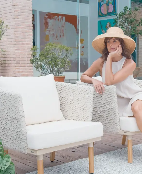 A square armchair in shades of white. It has a scaled texture and a padded seat. The legs are made of wood.