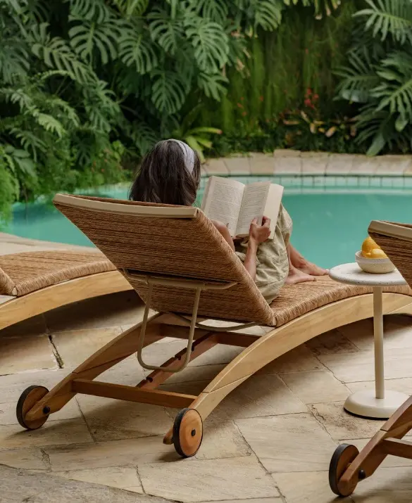 View from behind a banana-straw chaise longue. A woman is reading a book on the chaise.