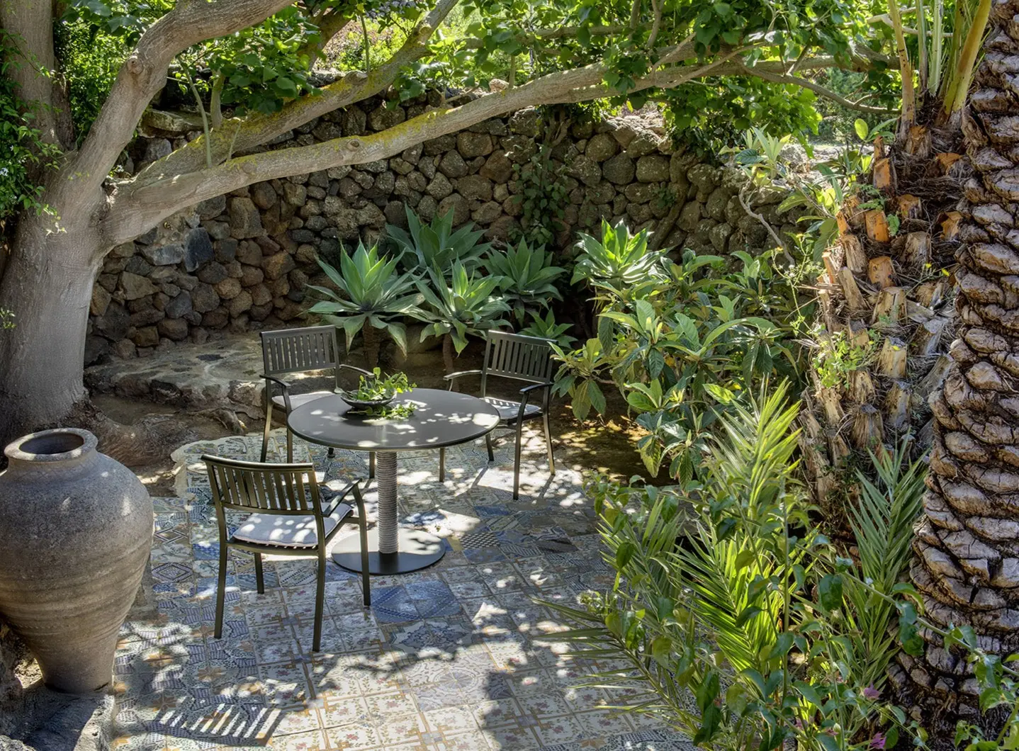 Noon table with round metal top and grey rope base, immersed in greenery.
