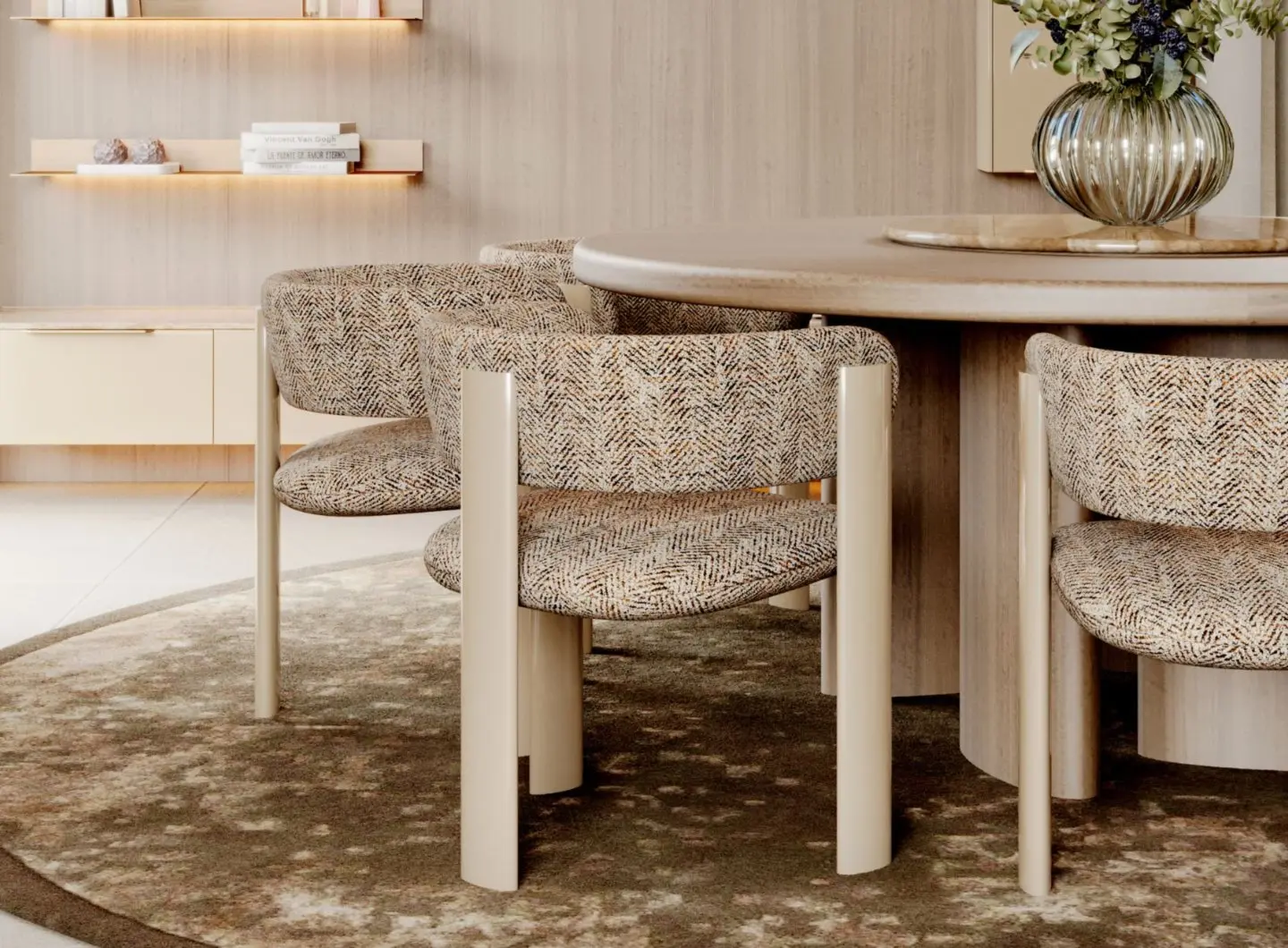The Dolomites Round Dining Table appears in a minimalist dining space with upholstered chairs featuring cylindrical legs, placed on an earthy-toned rug. A glass vase with flowers rests at the center, while warm wooden shelving and ambient lighting enhance the calm, cohesive atmosphere.