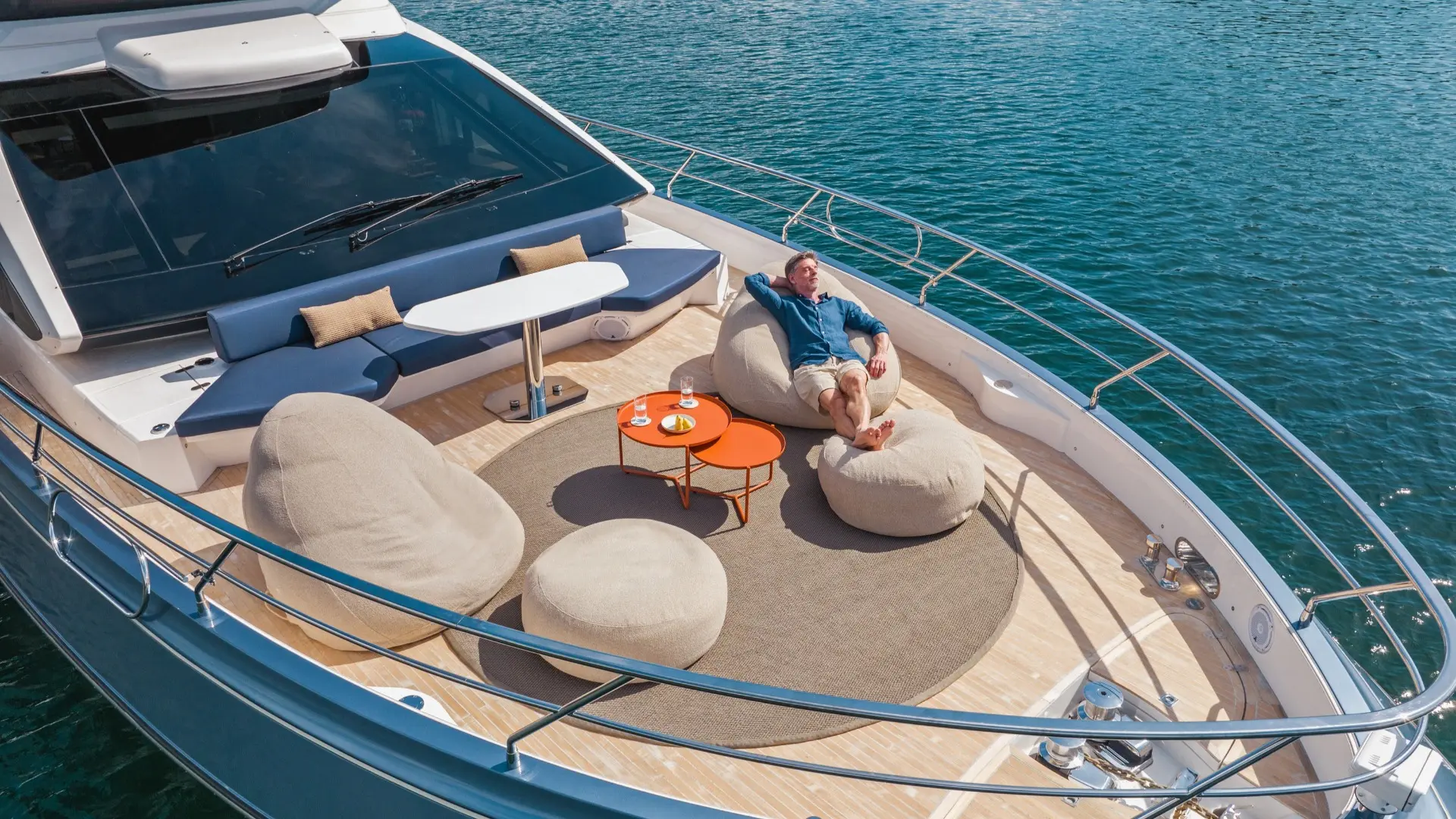 Uno yacht con due poltrone a sacco una accanto all'altra. Tra di esse, un tavolino arancione. Un signore è sdraiato rilassato su una delle poltrone a sacco. Lo yacht naviga su un mare blu intenso.
